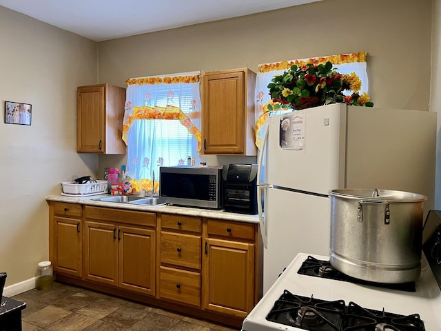 kitchen featuring white appliances, baseboards, brown cabinetry, light countertops, and a sink