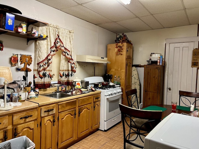 kitchen featuring a paneled ceiling, light countertops, a sink, white range with gas stovetop, and under cabinet range hood