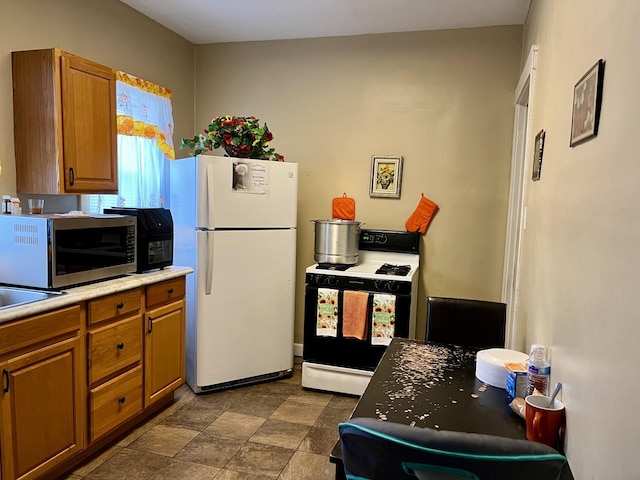 kitchen with range with gas stovetop, light countertops, freestanding refrigerator, brown cabinets, and stainless steel microwave