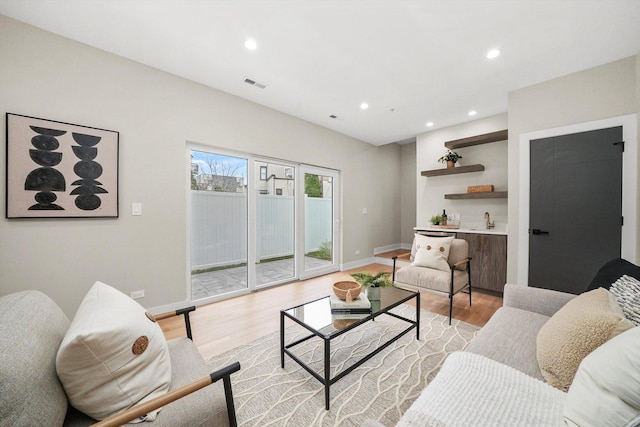 living area featuring visible vents, light wood finished floors, baseboards, recessed lighting, and bar