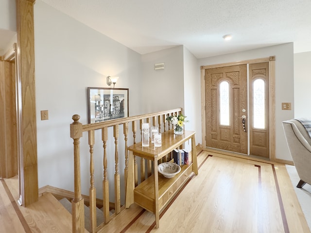 foyer featuring a textured ceiling, light wood-type flooring, and baseboards