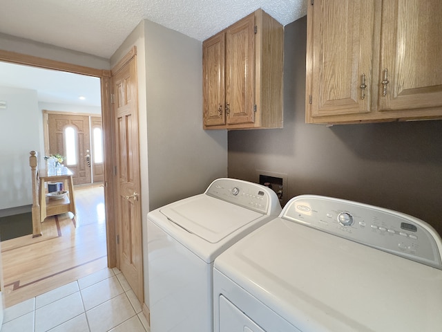 washroom with cabinet space, washer and clothes dryer, a textured ceiling, and light tile patterned floors