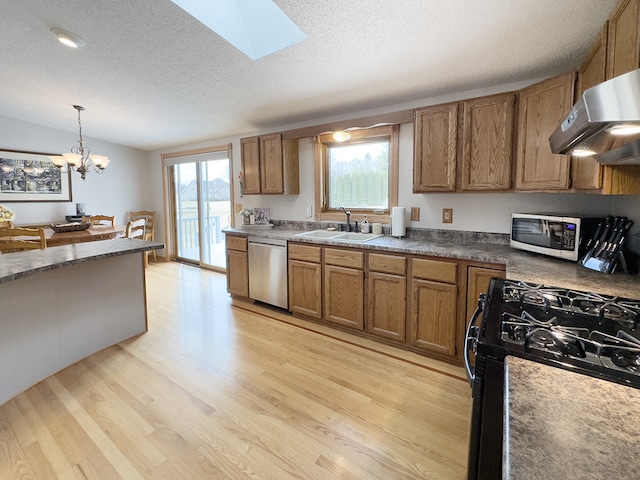 kitchen featuring appliances with stainless steel finishes, brown cabinetry, a healthy amount of sunlight, a sink, and light wood-type flooring