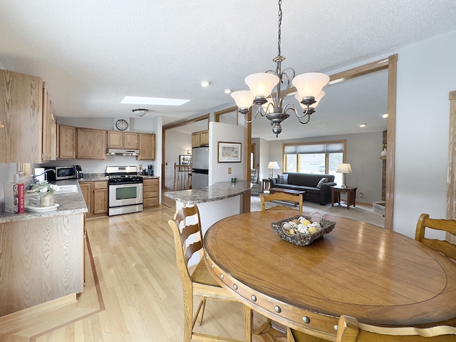 dining room with light wood-style floors, a chandelier, a textured ceiling, and lofted ceiling with skylight