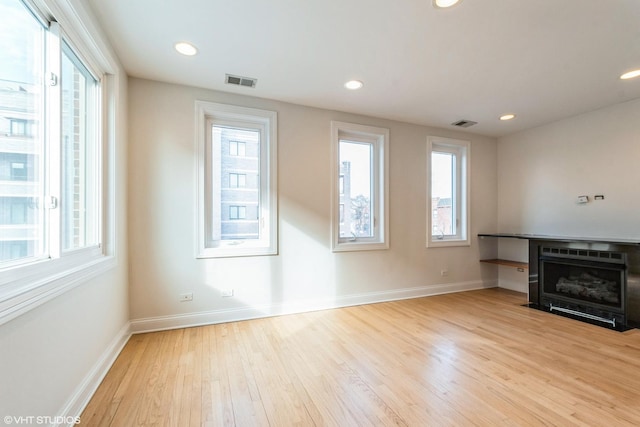 unfurnished living room with a healthy amount of sunlight, baseboards, visible vents, and wood finished floors