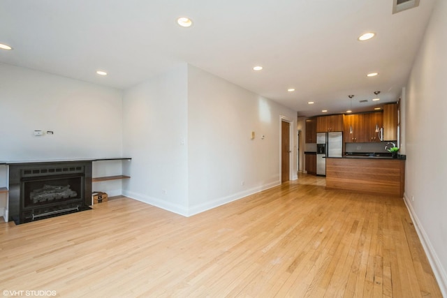 living area featuring recessed lighting, a fireplace with flush hearth, visible vents, baseboards, and light wood-style floors