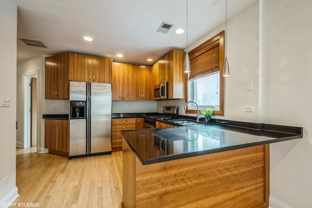 kitchen with stainless steel appliances, a peninsula, a sink, light wood-style floors, and brown cabinetry