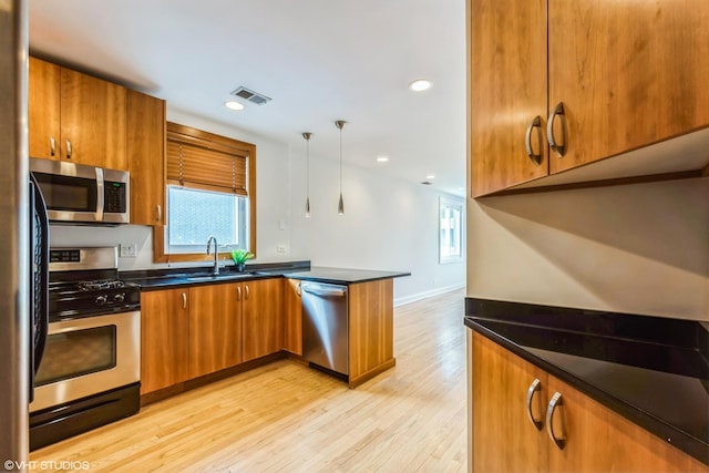 kitchen with light wood finished floors, visible vents, appliances with stainless steel finishes, brown cabinetry, and a peninsula