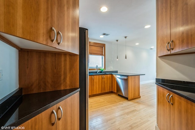 kitchen featuring light wood-style flooring, a peninsula, a sink, appliances with stainless steel finishes, and brown cabinets