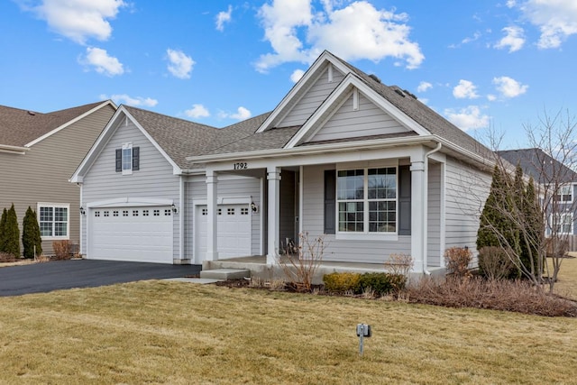 view of front of home with covered porch, roof with shingles, aphalt driveway, and a front lawn