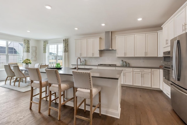 kitchen featuring wall chimney exhaust hood, appliances with stainless steel finishes, a sink, and dark wood finished floors