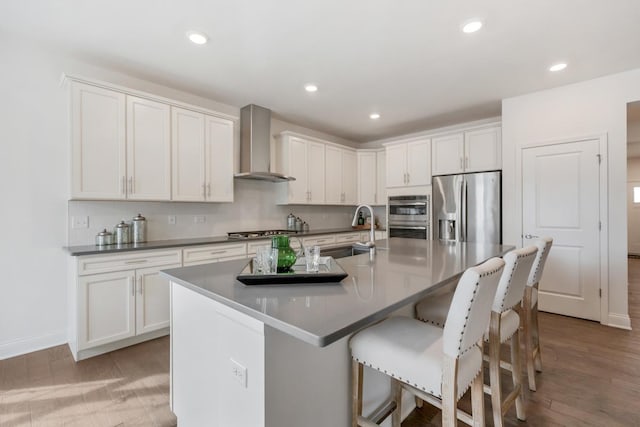 kitchen featuring stainless steel appliances, a kitchen bar, light wood-style flooring, a sink, and wall chimney exhaust hood