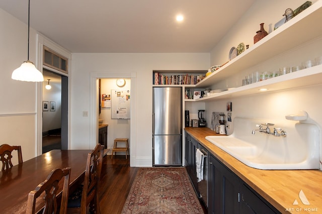 kitchen with decorative light fixtures, dark wood finished floors, wooden counters, a sink, and freestanding refrigerator
