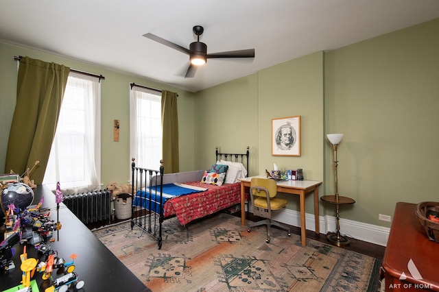 bedroom featuring radiator, wood finished floors, ceiling fan, and baseboards