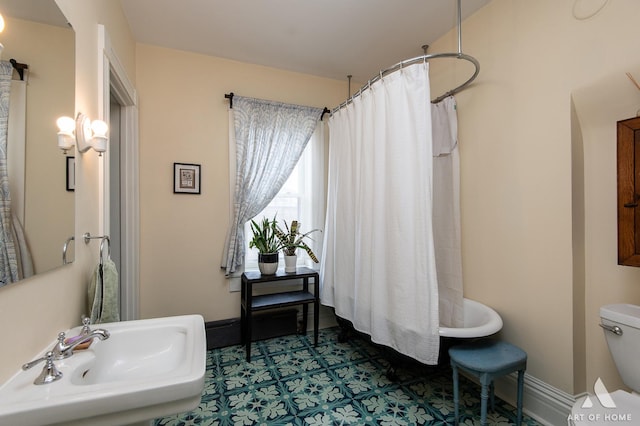 bathroom featuring baseboards, a shower with shower curtain, toilet, and a sink