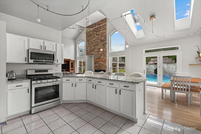 kitchen with light stone counters, a skylight, stainless steel appliances, white cabinetry, and a peninsula