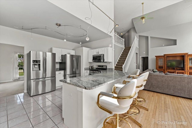 kitchen featuring light stone counters, stainless steel appliances, a high ceiling, white cabinets, and a peninsula