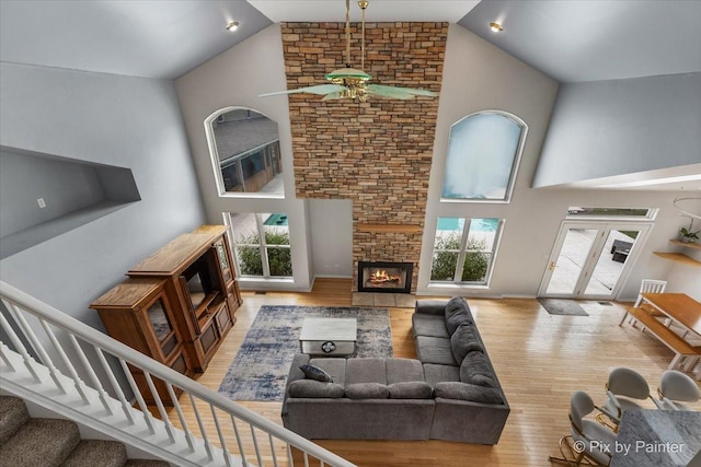 living room featuring high vaulted ceiling, a stone fireplace, stairway, and wood finished floors