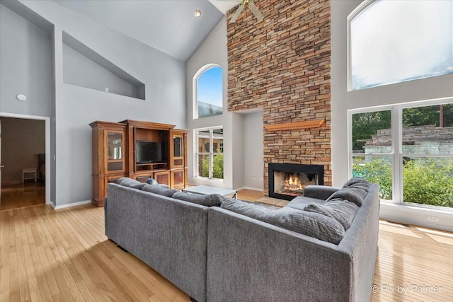 living area featuring high vaulted ceiling, a fireplace, light wood-style flooring, and baseboards