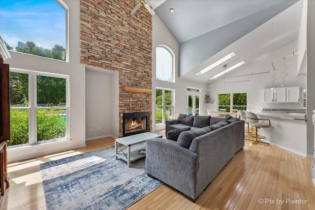 living room featuring light wood-type flooring, a skylight, high vaulted ceiling, and a stone fireplace