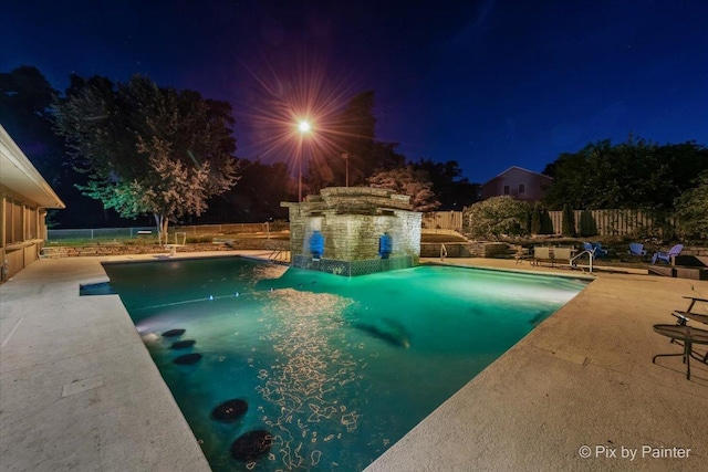 pool at night with a patio area, a fenced backyard, and a fenced in pool