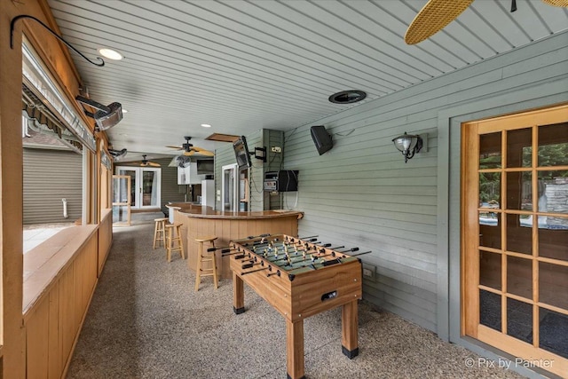 recreation room with carpet, ceiling fan, and wood walls