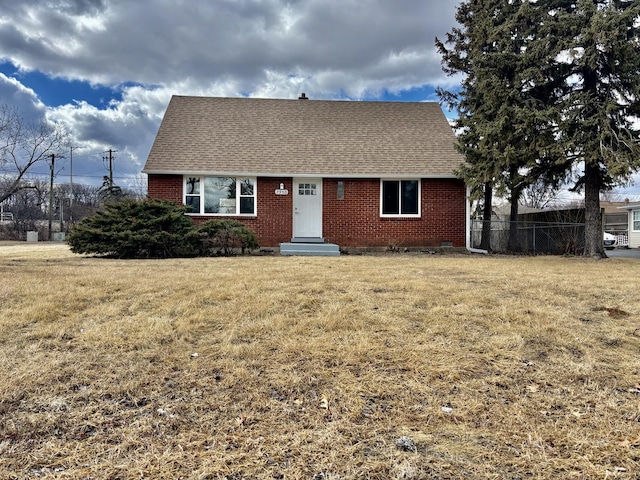 view of front of property with roof with shingles, a front yard, and brick siding