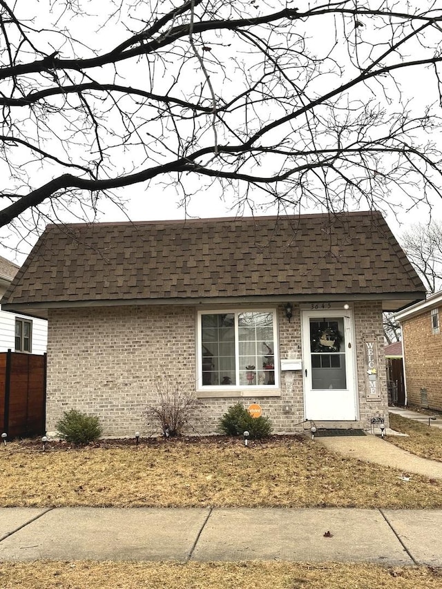 view of front of home with a shingled roof, brick siding, fence, and mansard roof