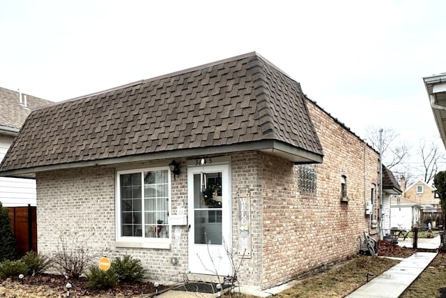 view of home's exterior featuring brick siding, mansard roof, and roof with shingles