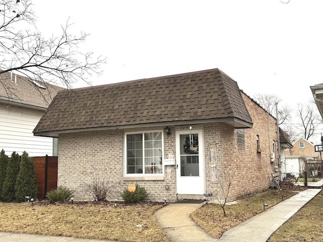 exterior space with a shingled roof, brick siding, fence, and mansard roof