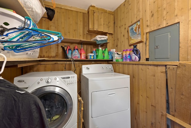 laundry area with laundry area, electric panel, wood walls, and separate washer and dryer