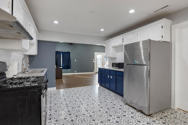 kitchen with visible vents, range with gas cooktop, freestanding refrigerator, blue cabinetry, and under cabinet range hood