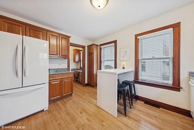 kitchen featuring light wood finished floors, baseboards, visible vents, brown cabinets, and freestanding refrigerator