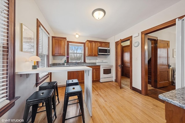 kitchen with white electric stove, a kitchen breakfast bar, brown cabinets, light wood finished floors, and stainless steel microwave