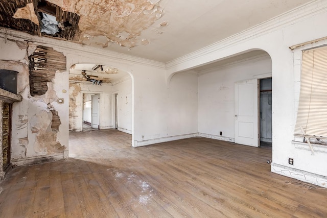 spare room with arched walkways, crown molding, and hardwood / wood-style flooring