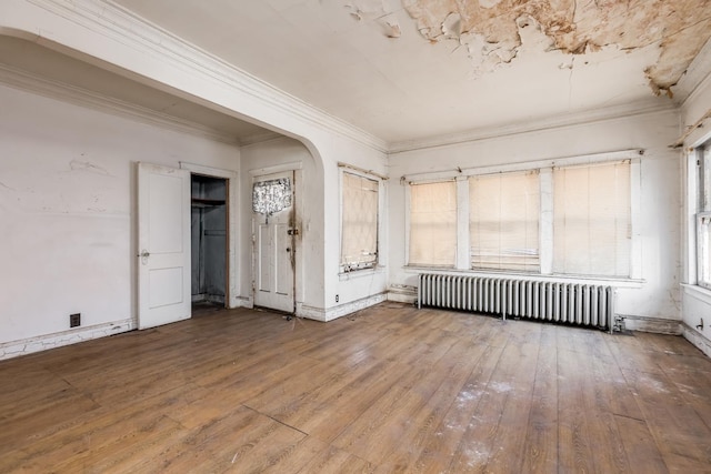 empty room featuring hardwood / wood-style flooring, radiator heating unit, arched walkways, and crown molding