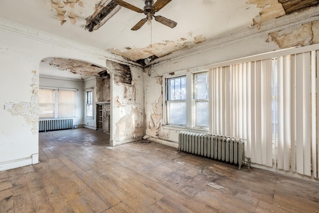 spare room with ornamental molding, arched walkways, radiator, and wood-type flooring