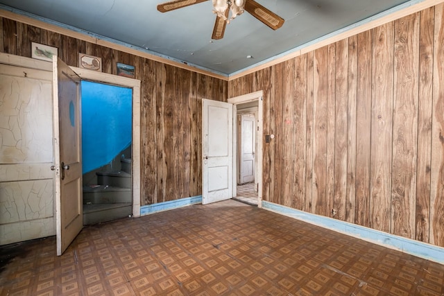 empty room with a ceiling fan, wooden walls, baseboards, and tile patterned floors