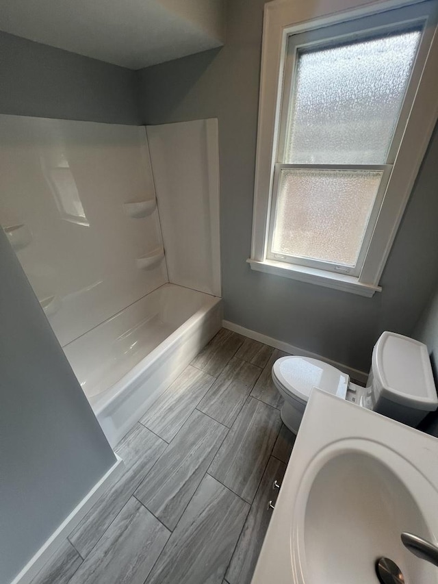 full bath with toilet, wood tiled floor, tub / shower combination, a sink, and baseboards