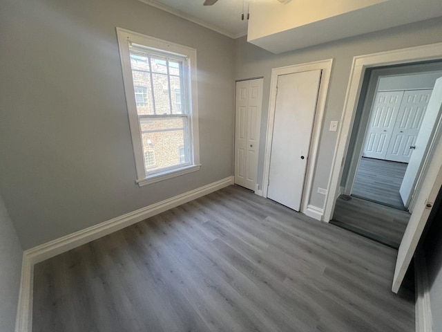 unfurnished bedroom with baseboards, ceiling fan, wood finished floors, crown molding, and two closets