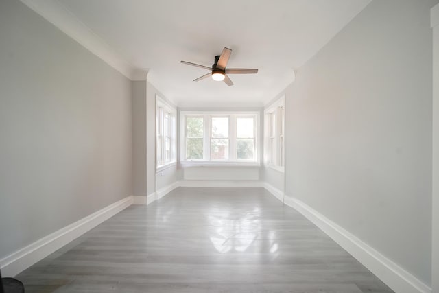 empty room with ornamental molding, wood finished floors, a ceiling fan, and baseboards