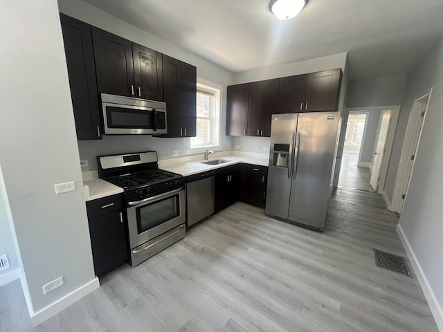 kitchen featuring light wood finished floors, stainless steel appliances, light countertops, visible vents, and a sink