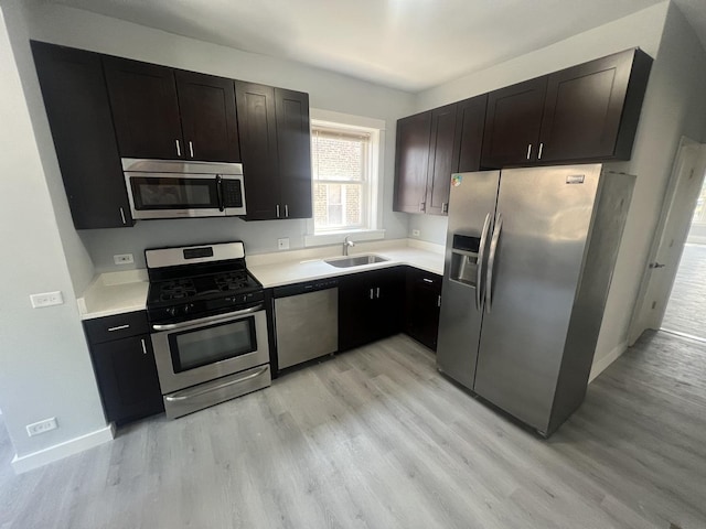 kitchen featuring stainless steel appliances, a sink, baseboards, light wood-style floors, and light countertops