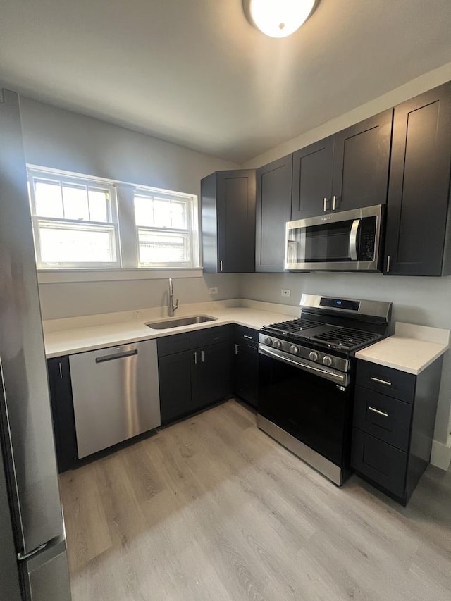 kitchen with light wood-style flooring, appliances with stainless steel finishes, light countertops, and a sink