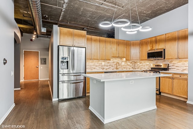 kitchen with dark wood-type flooring, a center island, appliances with stainless steel finishes, light countertops, and decorative backsplash