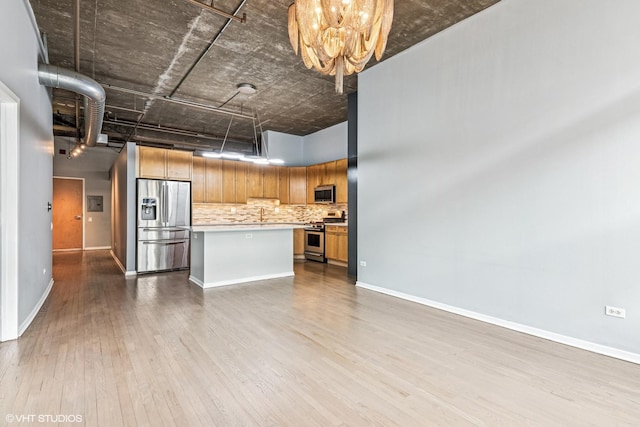 kitchen with wood finished floors, stainless steel appliances, decorative backsplash, light countertops, and a center island