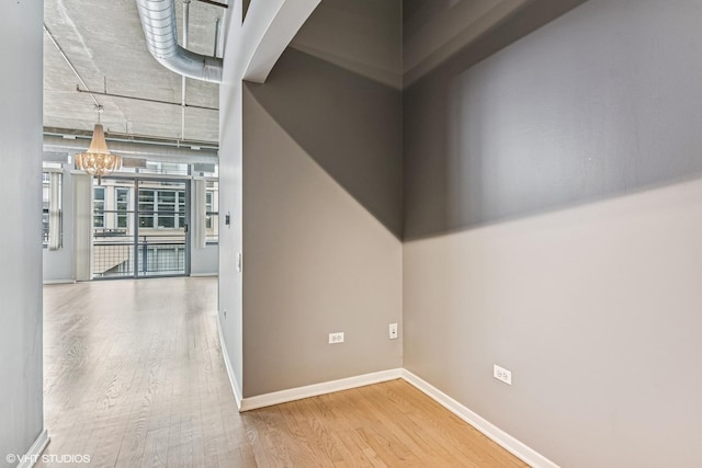 hallway featuring baseboards, a notable chandelier, and wood finished floors