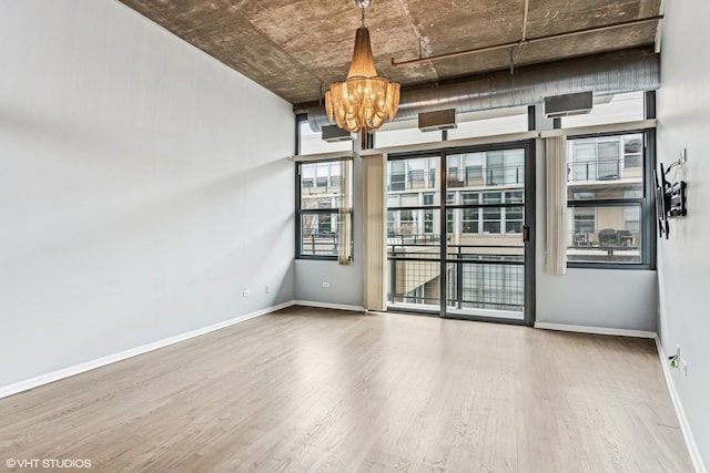 empty room with baseboards, an inviting chandelier, and wood finished floors