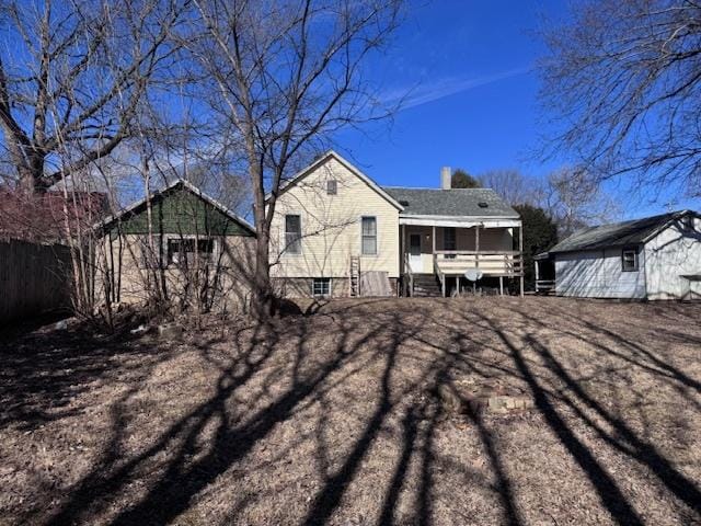 rear view of property featuring a chimney, covered porch, fence, an outdoor structure, and a shed