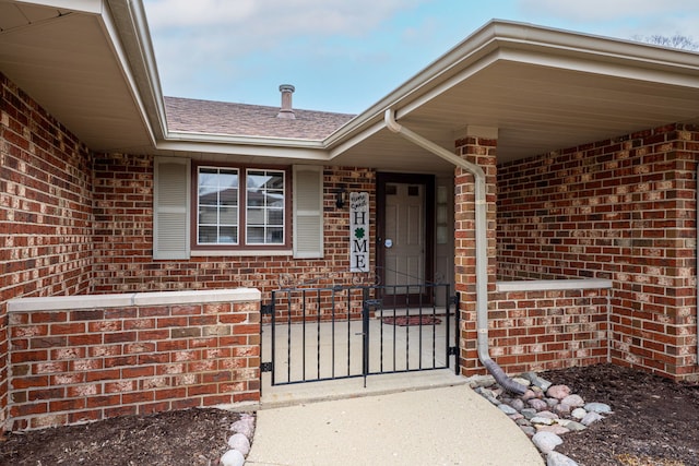 entrance to property featuring brick siding and roof with shingles